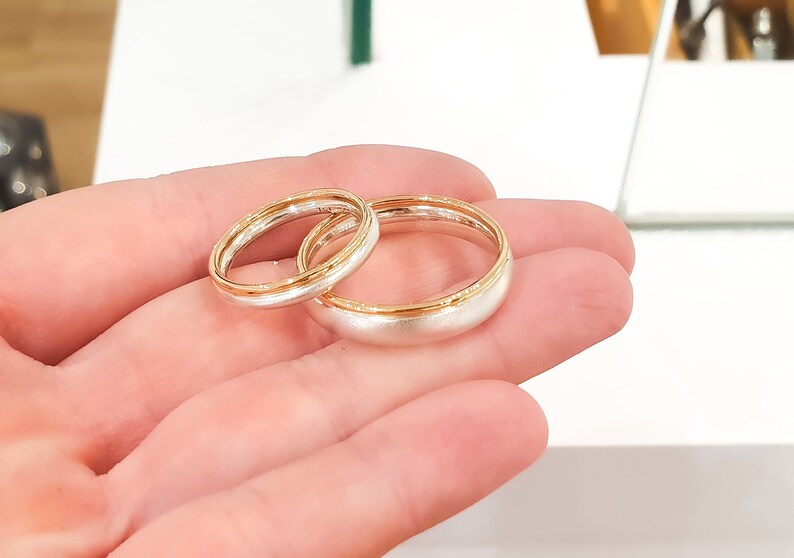 May include: Two wedding bands, one with a gold band and the other with a silver band.