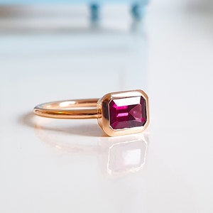 Könnte beinhalten: Ein Ring aus Roségold mit einem tief roten, smaragdgeschliffenen Edelstein.