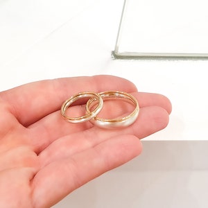 May include: Two wedding bands, one silver and one gold, are displayed on a hand. The bands are both simple and elegant.
