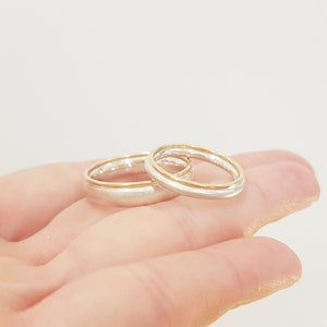 May include: Two wedding bands, one silver and one gold, are stacked on top of each other. The bands are both simple and elegant.