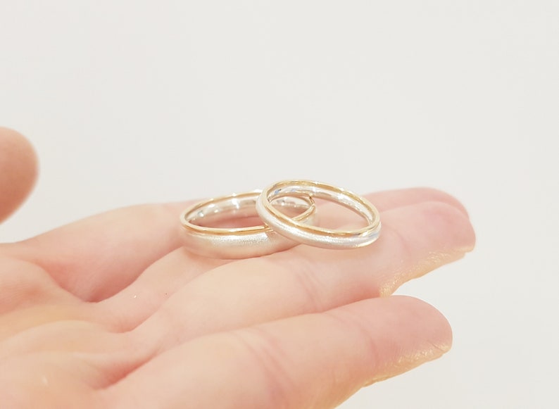 May include: Two wedding bands, one silver and one gold, are stacked on top of each other. The bands are both simple and elegant.