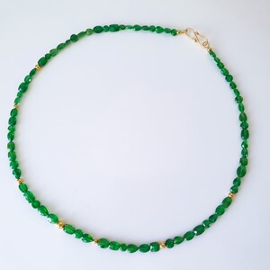 Pu&ograve; includere: Una collana di pietre preziose verdi con perline dorate. La collana &egrave; realizzata con pietre verdi di forma ovale e piccole perline dorate.
