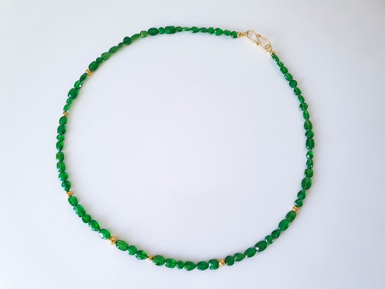 Pu&ograve; includere: Una collana di pietre preziose verdi con perline dorate. La collana &egrave; realizzata con pietre verdi di forma ovale e piccole perline dorate.