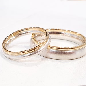 May include: Two wedding bands, one with a gold band and the other with a silver band.