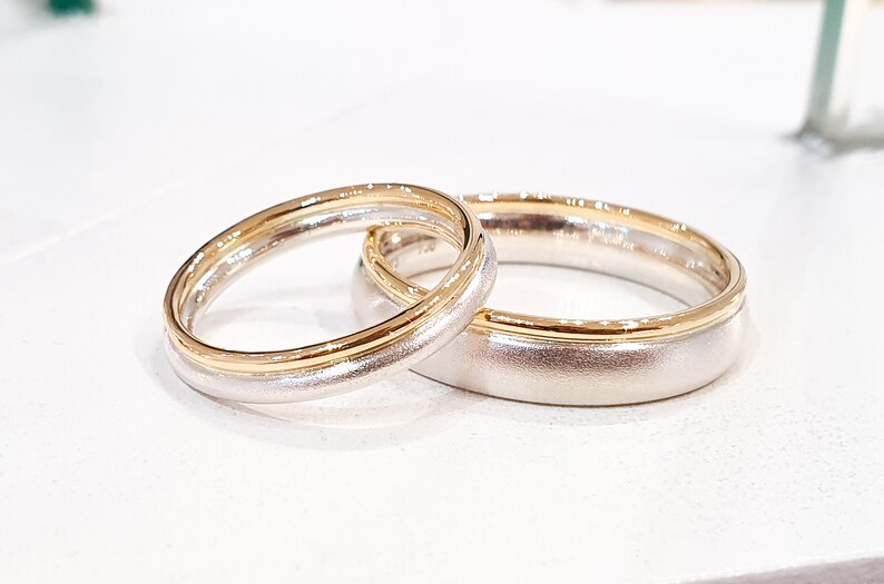 May include: Two wedding bands, one with a gold band and the other with a silver band.