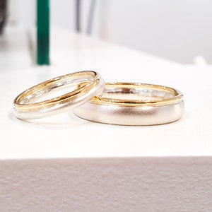 May include: Two wedding bands, one with a gold band and the other with a silver band.