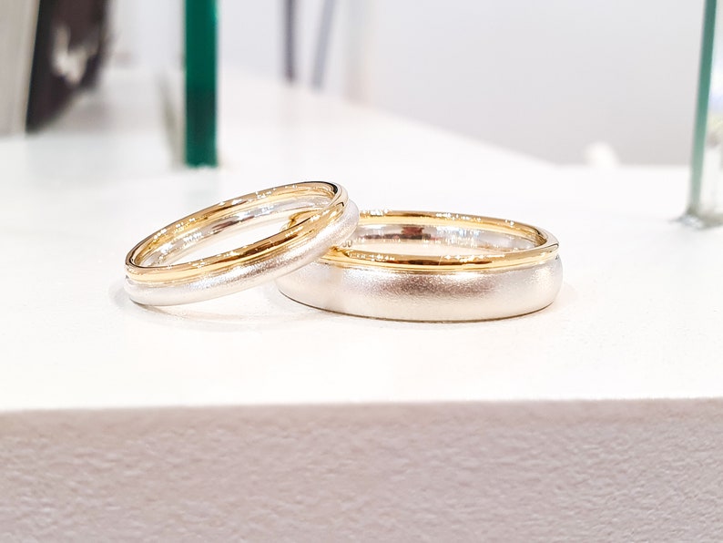 May include: Two wedding bands, one with a gold band and the other with a silver band.