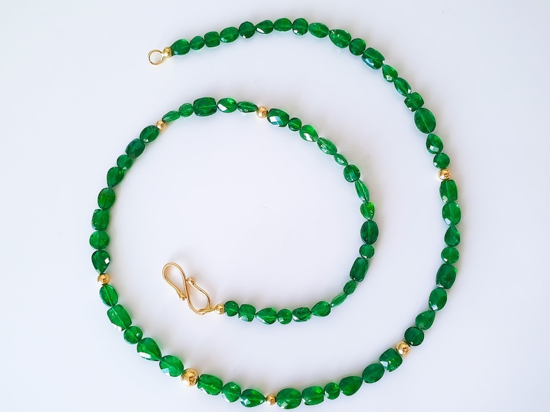 Pu&ograve; includere: Una collana di pietre preziose verdi con accenti dorati. La collana &egrave; realizzata con pietre verdi di forma ovale e perline dorate.