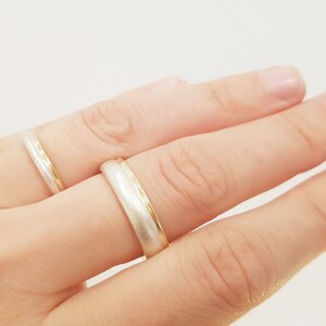 May include: Two wedding bands on a finger. One band is silver with a gold edge, and the other is gold with a silver edge.