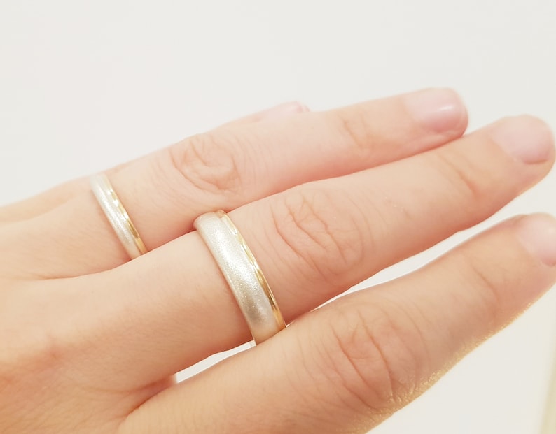 May include: Two wedding bands on a finger. One band is silver with a gold edge, and the other is gold with a silver edge.