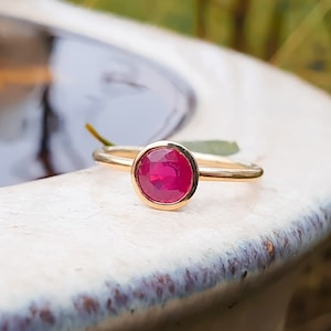 Könnte beinhalten: Ein goldener Ring mit einem runden, gefassten Rubin-Edelstein. Der Rubin hat eine tiefrote Farbe.
