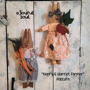 Könnte beinhalten: Zwei handgefertigte Stoffhasenpuppen, eine mit Karotten und die andere mit einer Rübe. Die Hasen tragen Latzhosen und ein Blumenkleid. Der Text "Henry & Harriet Farmer Pattern" ist sichtbar.