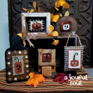 May include: A collection of handmade Halloween decorations featuring pumpkin designs. Includes a framed piece, a wooden slice, a cutting board, and small fabric pieces. The decorations are in shades of orange, brown, and black, with button and fabric accents.