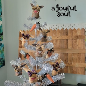 May include: A decorative Easter tree with silver tinsel branches, adorned with fabric bunny ornaments and carrot decorations. The tree is set against a light-colored wall with the text "a joyful Soul".