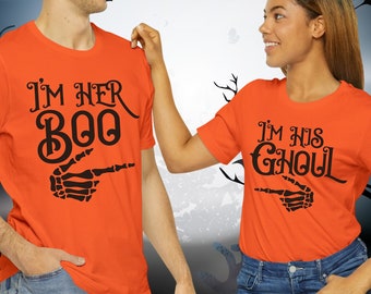 May include: Couple wearing matching orange t-shirts with a skeleton hand graphic and text that reads "I'm her Boo" and "I'm his Ghoul".