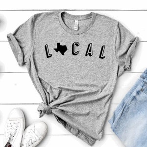 May include: A gray t-shirt with a black graphic of the state of Texas and the word "LOCAL" in block letters.