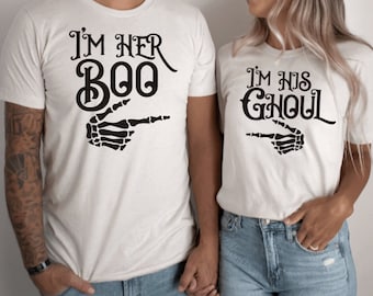 May include: Two white t-shirts with black text and skeleton hand graphics. The text on the first shirt reads "I'm her Boo" and the text on the second shirt reads "I'm his Ghoul".