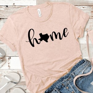 May include: A pink t-shirt with a black graphic of the state of Texas and the word "home" in cursive.