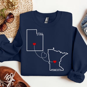 May include: Navy blue sweatshirt with a white outline of Utah and Minnesota with a red heart in each state and a dotted line connecting the two states. The text "Utah" and "Minnesota" are written below each state.