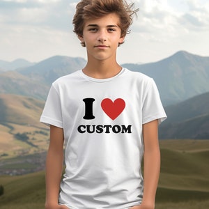 Puede incluir: Camiseta blanca con un gr&aacute;fico negro "I love" y un coraz&oacute;n rojo. El texto "CUSTOM" est&aacute; impreso en negro debajo del coraz&oacute;n.