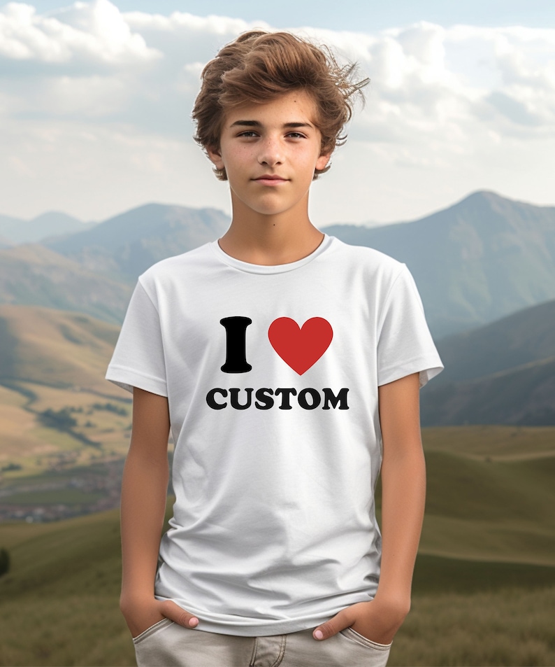 Puede incluir: Camiseta blanca con un gr&aacute;fico negro "I love" y un coraz&oacute;n rojo. El texto "CUSTOM" est&aacute; impreso en negro debajo del coraz&oacute;n.