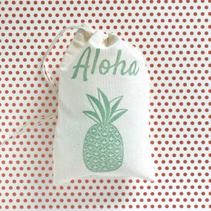 May include: A white drawstring bag with a green pineapple and the word "Aloha" printed on it. The bag is on a red polka dot background.