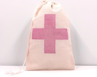 May include: A beige drawstring pouch made of a woven fabric featuring a large, centered pink cross graphic. The bag is closed at the top with thin, matching beige fabric cords that extend from the sides, creating a simple and functional storage item.