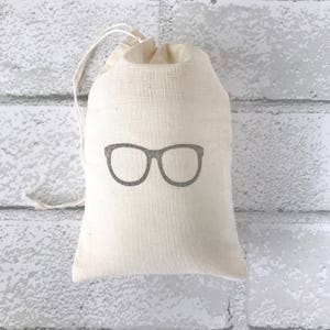 Könnte beinhalten: Eine kleine, weiße Baumwolltasche mit Kordelzug und einem grauen Umriss einer Brille auf der Vorderseite.