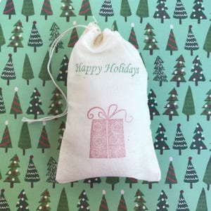 May include: A white cotton drawstring bag with the text "Happy Holidays" printed on the front. A pink gift box with a bow is printed on the bag.