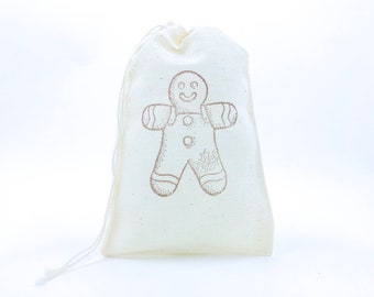 Könnte beinhalten: Eine weiße Baumwolltasche mit Kordelzug und einem aufgedruckten Lebkuchenmann-Motiv auf der Vorderseite. Der Lebkuchenmann ist braun und hat ein lächelndes Gesicht.