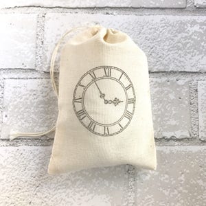 Può includere: Una borsa di cotone bianco con coulisse e un design a orologio nero. Il quadrante dell'orologio ha numeri romani e un design semplice.