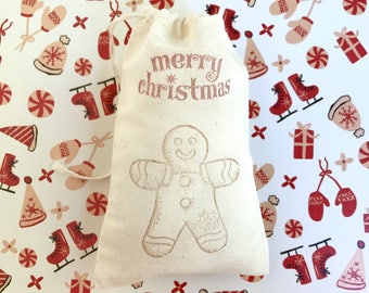 Könnte beinhalten: Ein weißer Stoff-Geschenkbeutel mit Kordelzug. Der Beutel hat eine rote Aufschrift "merry christmas" und eine Lebkuchenmann-Grafik auf der Vorderseite.