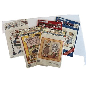 May include: Four iron-on transfer designs by Daisy Kingdom featuring artwork by Mary Engelbreit. The designs include a girl with a watering can, a girl with a bird, a girl with a flower pot, and a girl with a dog. The designs are all in a whimsical style with bright colors and bold outlines.