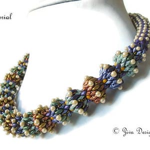 Könnte beinhalten: Eine mehrfarbige Perlenkette mit einem Spiraldesign. Die Perlen sind in Blautönen, Lila, Grün, Gold und Weiß. Die Kette liegt auf einem weißen Hintergrund.