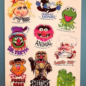 May include: A set of ten Muppet character stickers featuring Miss Piggy, The Great Gonzo, Kermit the Frog, Dr. Teeth, Animal, Swedish Chef, Fozzie Bear, Sweetums, and Robin. The stickers are printed on white paper with a blue background.