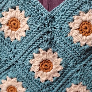 May include: A crocheted bag with a blue background and white daisy flowers with brown centers.