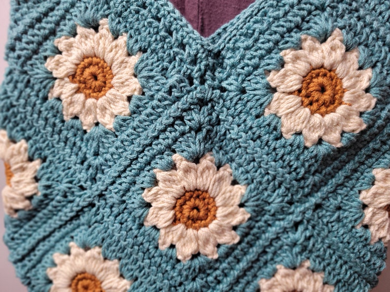 May include: A crocheted bag with a blue background and white daisy flowers with brown centers.