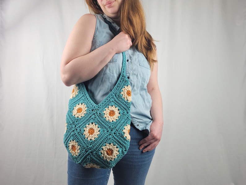 May include: A teal crocheted tote bag with a daisy pattern. The bag has a long strap and is worn over the shoulder.