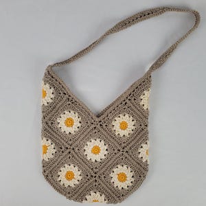 May include: A crocheted shoulder bag with a daisy pattern in beige and yellow.