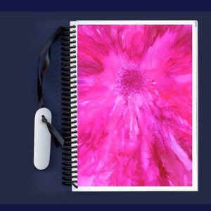 May include: A pink spiral bound notebook with a black ribbon bookmark. The cover features a pink abstract flower design.
