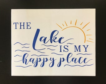 May include: White wooden sign with blue and gold lettering. The sign reads "The lake is my happy place".
