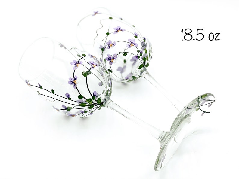 K&ouml;nnte beinhalten: Zwei handbemalte Weingl&auml;ser mit lila Blumen und gr&uuml;nen Bl&auml;ttern. Die Gl&auml;ser haben ein Fassungsverm&ouml;gen von 18,5 oz.