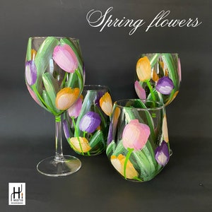 May include: Four wine glasses painted with spring flowers. The glasses feature a design of pink, yellow, and purple tulips with green leaves.