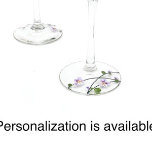 K&ouml;nnte beinhalten: Zwei klare Weingl&auml;ser aus Glas mit einem floralen Design. Das Design zeigt lila Blumen und gr&uuml;ne Bl&auml;tter. Personalisierung ist m&ouml;glich.