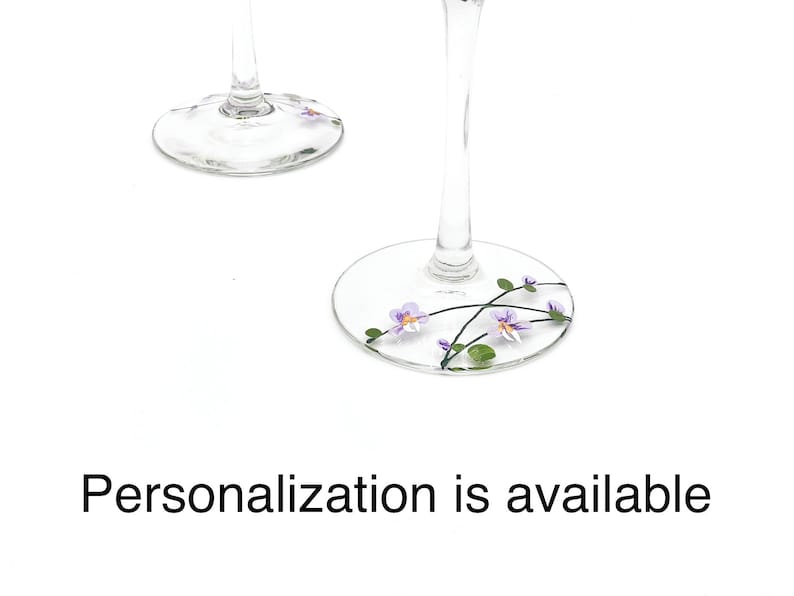 K&ouml;nnte beinhalten: Zwei klare Weingl&auml;ser aus Glas mit einem floralen Design. Das Design zeigt lila Blumen und gr&uuml;ne Bl&auml;tter. Personalisierung ist m&ouml;glich.