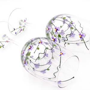 K&ouml;nnte beinhalten: Zwei klare Weingl&auml;ser aus Glas mit purpurfarbenen und gr&uuml;nen Blumenmustern, die auf das Glas gemalt sind.