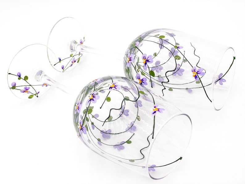 K&ouml;nnte beinhalten: Zwei klare Weingl&auml;ser aus Glas mit purpurfarbenen und gr&uuml;nen Blumenmustern, die auf das Glas gemalt sind.