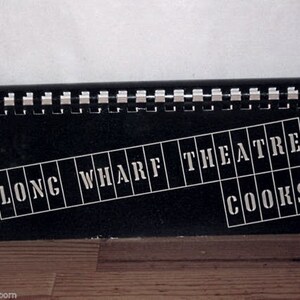Puede incluir: Un letrero en blanco y negro con las palabras "Long Wharf Theatre" y "Cooks" en letras blancas.