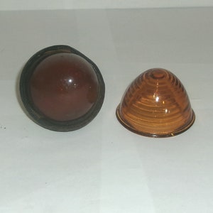 May include: Two amber colored car lights. One is round and has a black rubber rim. The other is a dome shape with a ribbed surface.