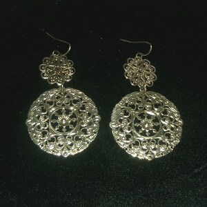 May include: A pair of silver filigree earrings with a circular design. The earrings have a delicate, intricate pattern and are perfect for adding a touch of elegance to any outfit.